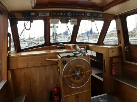 Nauticat 33: varnished wooden wheelhouse with central wheel, roof-mounted instruments and marina view