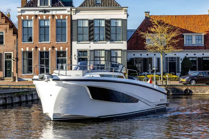 Delphia 10 Lounge: bow view of the white hull underway on a canal lined with brick houses