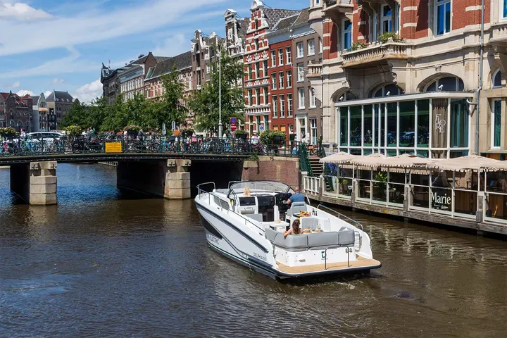 Delphia 10 Lounge: stern view cruising along a city canal towards a bridge, people seated in cockpit