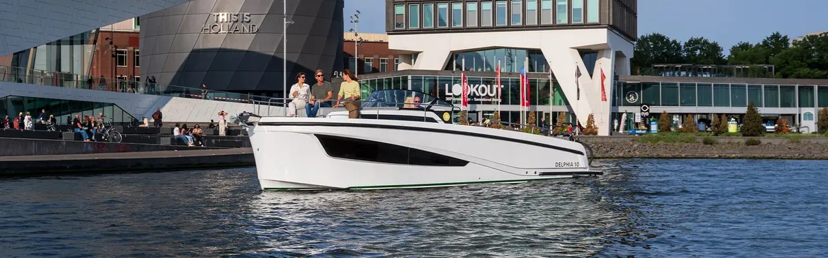 Delphia 10 Lounge: white motorboat cruising past modern waterfront buildings with four people standing at the helm