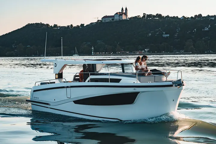 Delphia 10 LoungeTop: boat cruising on a lake with people on the foredeck sunpad and at the helm, hillside behind