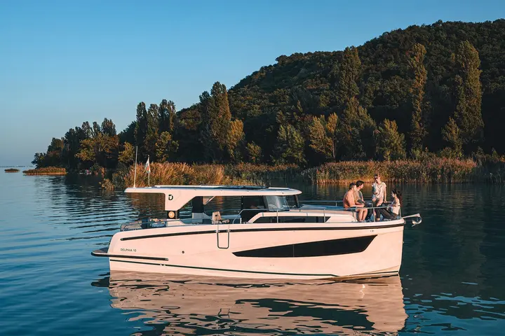 Delphia 10 LoungeTop: boat at rest near a wooded shore, four people relaxing on the foredeck