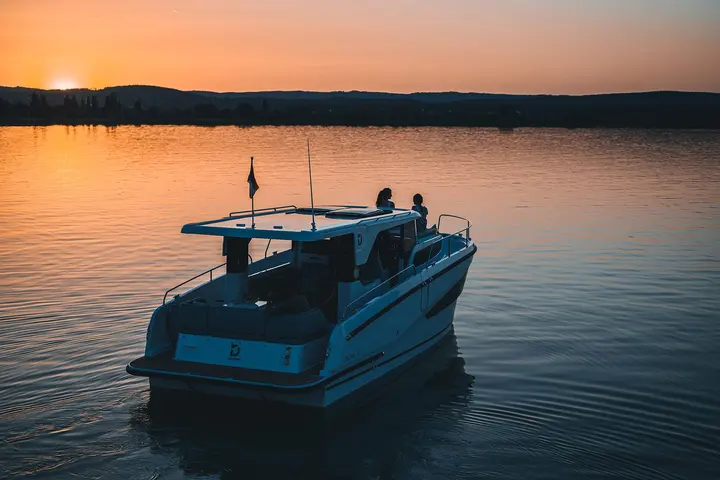 Delphia 10 LoungeTop: boat viewed from astern at sunset, two people standing on the hardtop roof