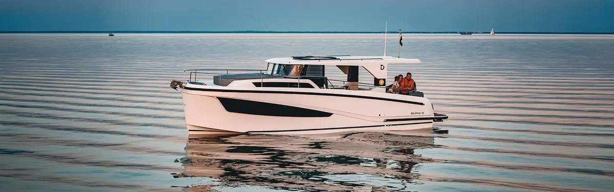 Delphia 10 LoungeTop: white motor cruiser with hardtop underway on calm water, two people seated in the aft cockpit
