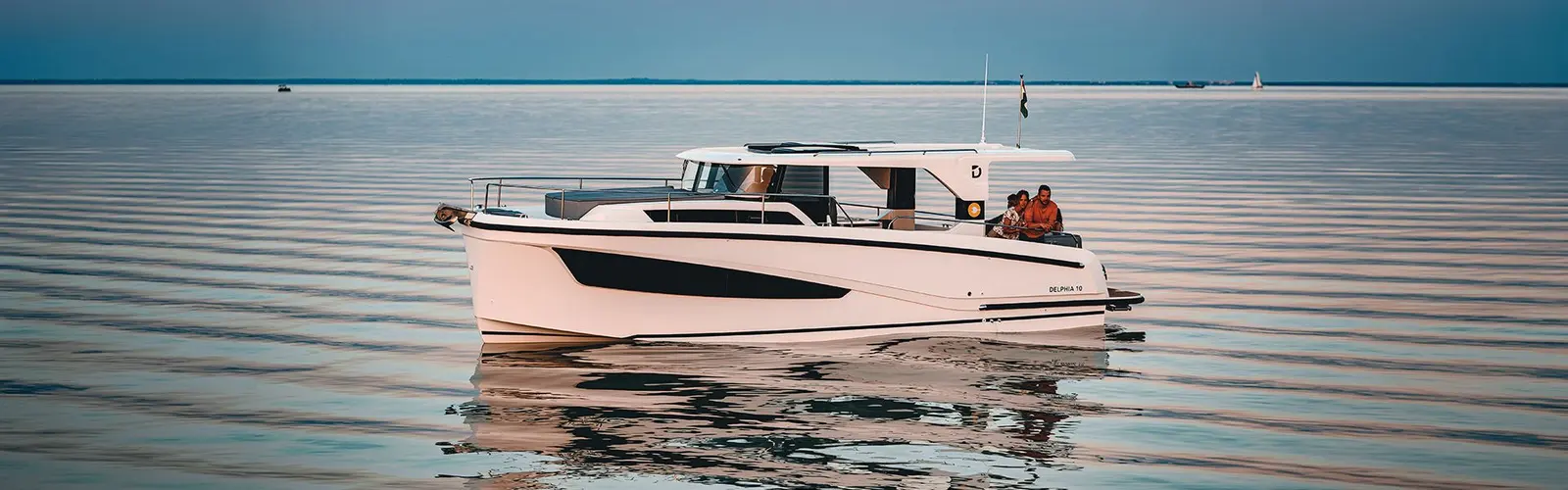 Delphia 10 LoungeTop: white motor cruiser with hardtop underway on calm water, two people seated in the aft cockpit