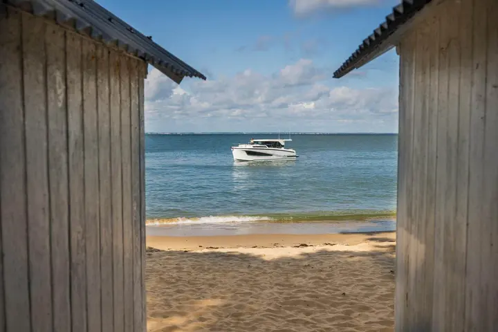 Delphia 10 Sedan: boat at anchor offshore, seen between two wooden beach huts across the sand