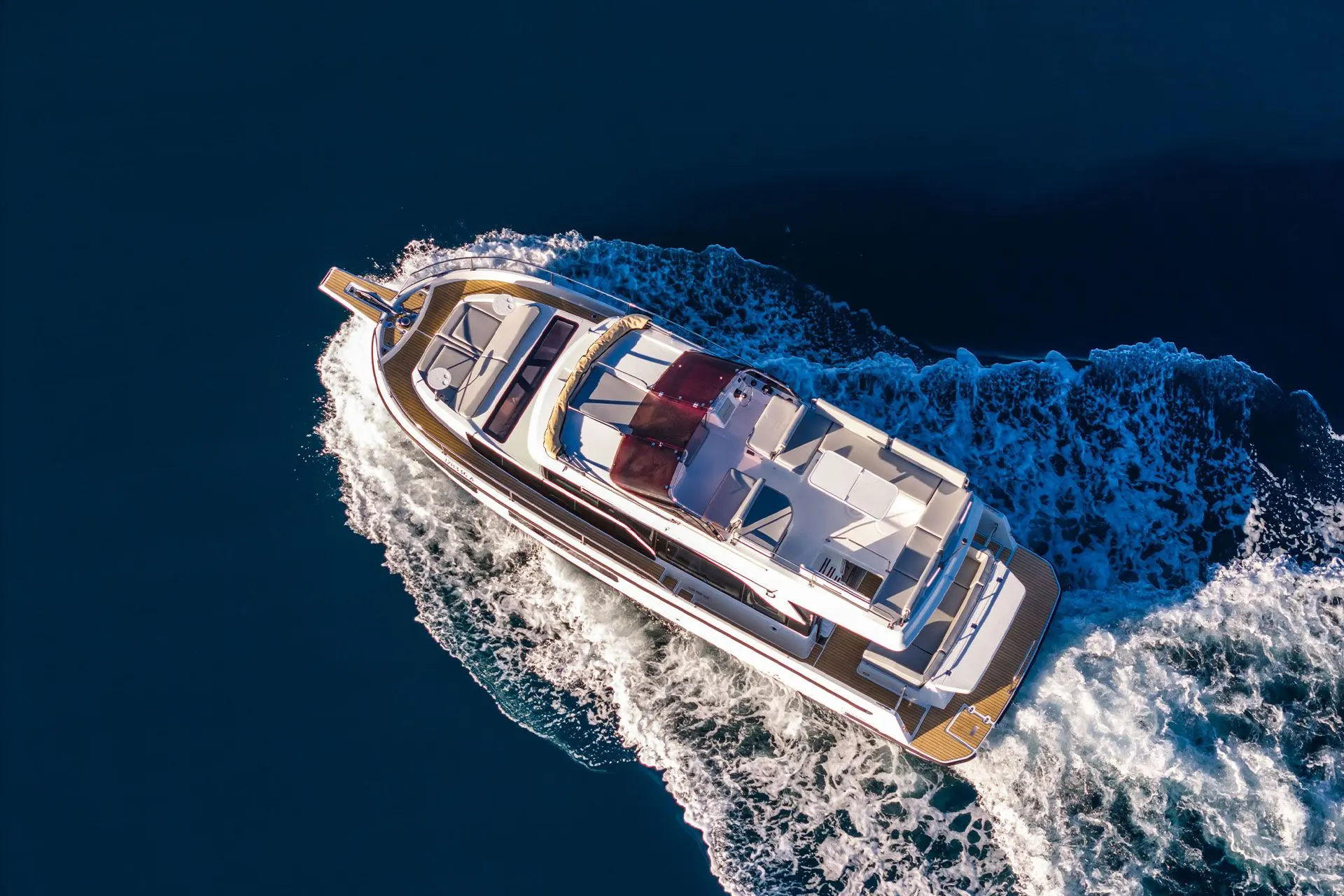 Delphia 11 FlyLounge: aerial view from above showing flybridge seating, red sunpads and teak side decks underway