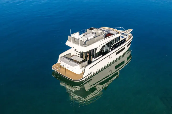 Delphia 11 FlyLounge: aerial stern view at anchor showing teak bathing platform, cockpit table and flybridge seating