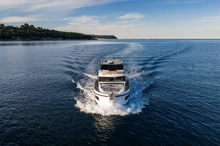 Delphia 11 FlyLounge: bow view of the motor yacht underway on calm blue water, leaving a white wake
