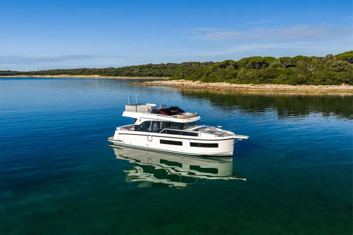 Delphia 11 FlyLounge: motor yacht at anchor in clear calm water off a wooded shoreline, reflection below