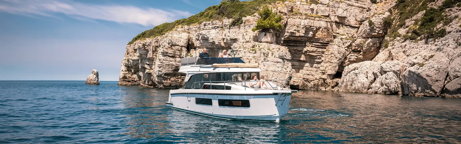 Delphia 11 FlyLounge: motor yacht cruising beside white limestone cliffs, guests on the flybridge and foredeck