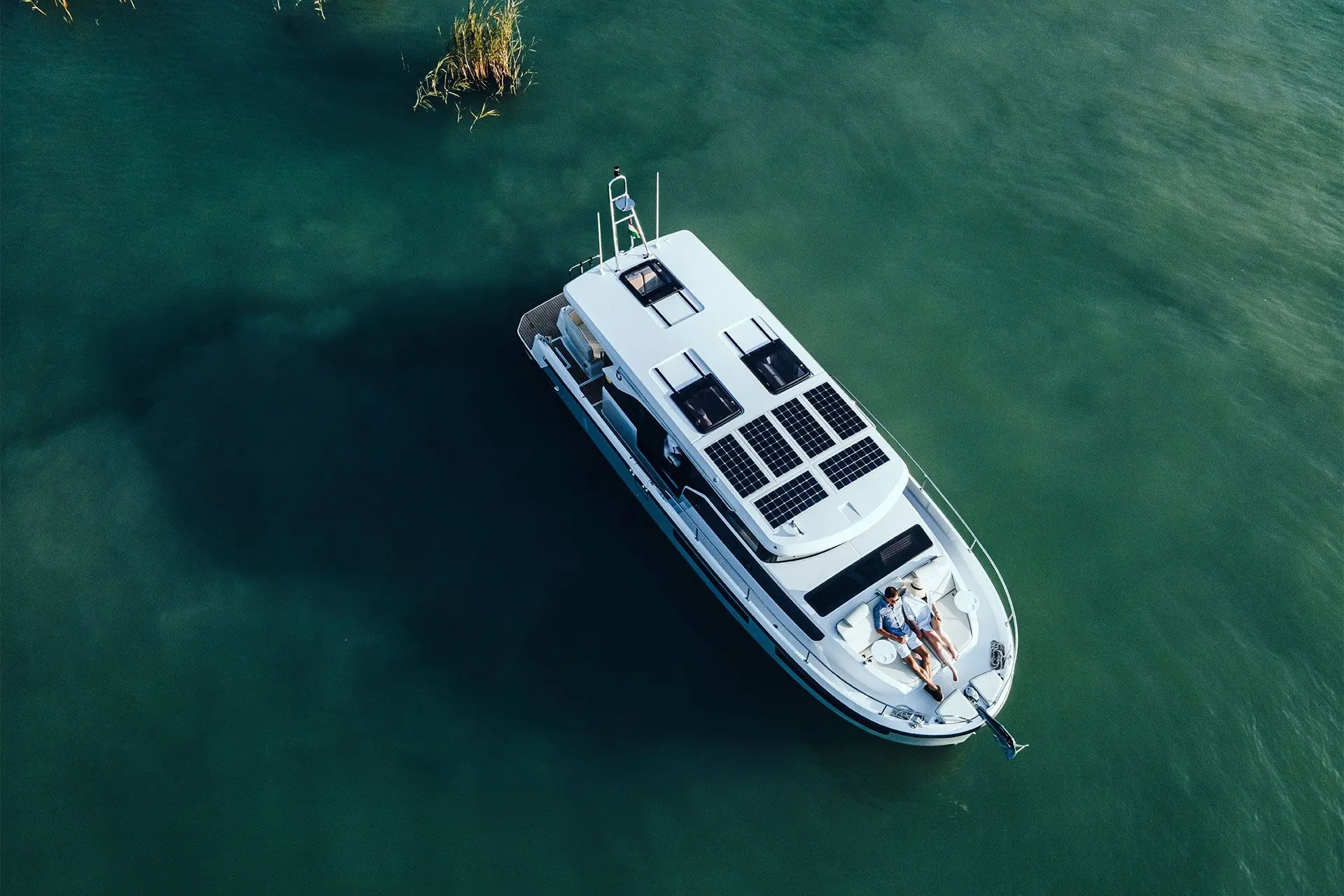 Delphia 11 Sedan: aerial view of the boat on green water, showing solar panels and hatches on the roof and two people on the foredeck