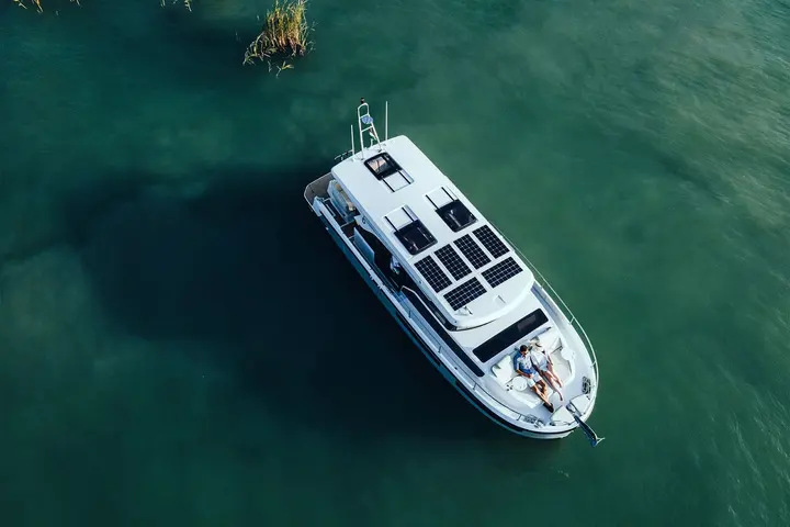 Delphia 11 Sedan: aerial view of the boat on green water, showing solar panels and hatches on the roof and two people on the foredeck