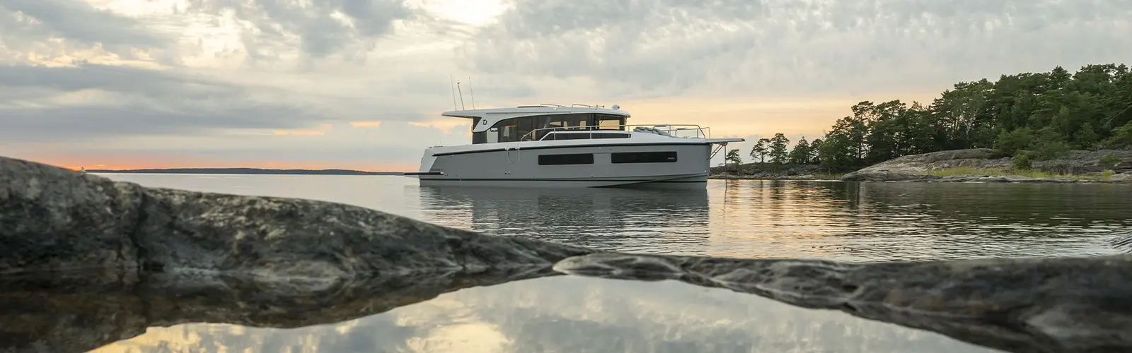 Delphia 11 Sedan: motor cruiser at anchor in a calm rocky bay at sunset, seen from the shoreline rocks