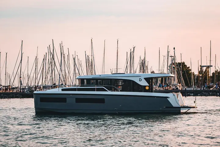Delphia 11 Sedan: side profile of the boat cruising past a marina full of sailing yacht masts at dusk