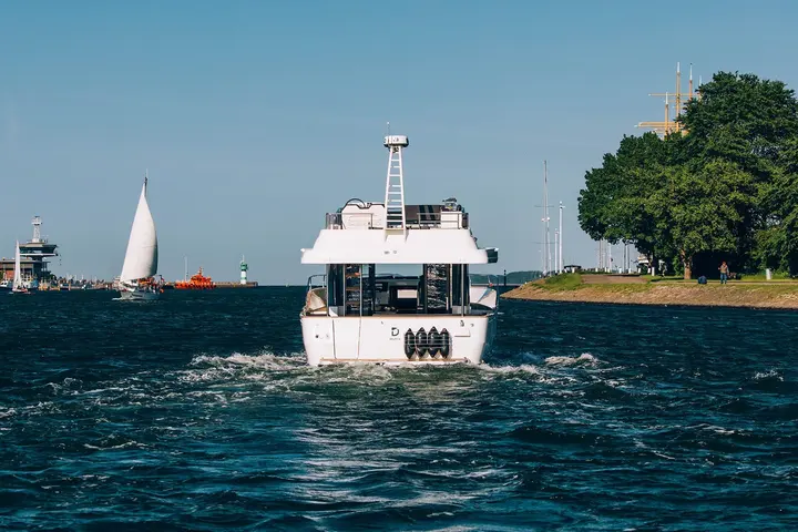 Delphia 12 FlyLounge: stern view of the yacht under way in a harbour entrance, with a sailing boat nearby
