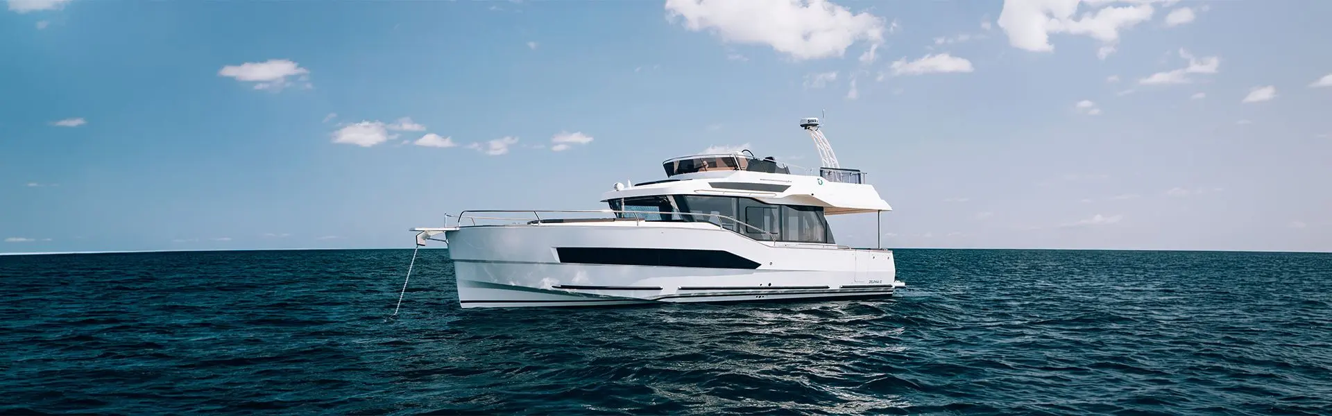 Delphia 12 FlyLounge: white motor yacht with flybridge lying at anchor on open sea under a blue sky