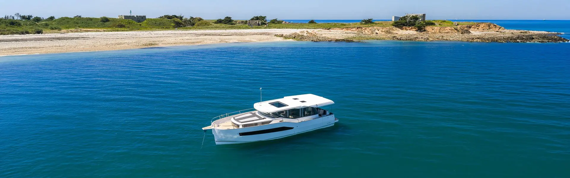 Delphia 12 Sedan: aerial view of the motor yacht at anchor in a calm blue bay near a sandy shore