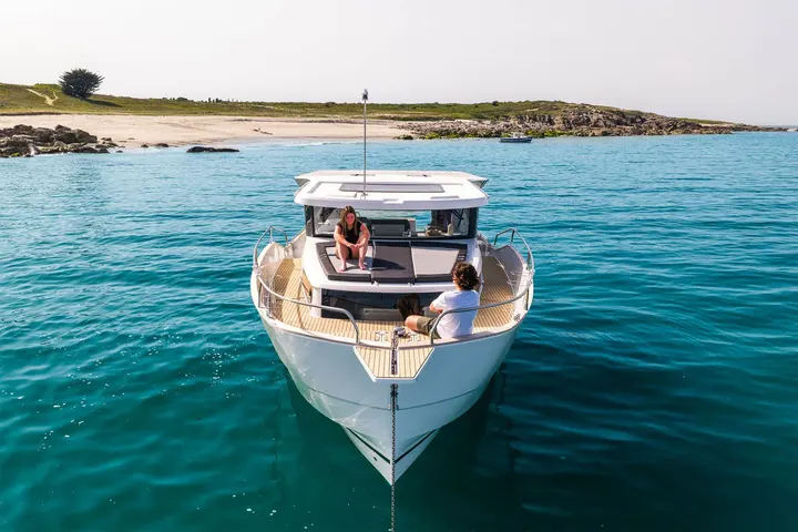 Delphia 12 Sedan: bow view at anchor showing teak foredeck, sunbed and two people seated forward