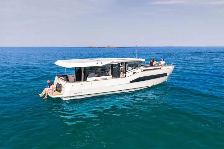 Delphia 12 Sedan: side view at anchor with people on the bathing platform and the forward sunbed