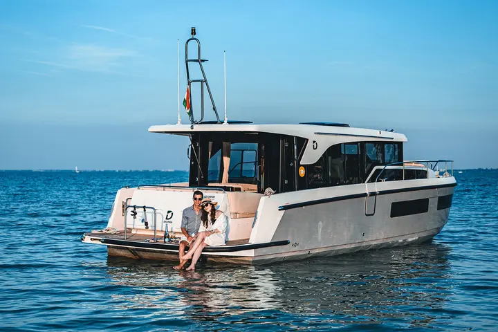 Delphia 11 Sedan: stern quarter view of the boat on open water with a couple sitting on the bathing platform