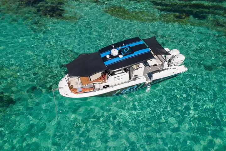 Jeanneau Cap Camarat 10.5 CC: aerial view at anchor in clear turquoise water, black hardtop with side shades and twin outboards