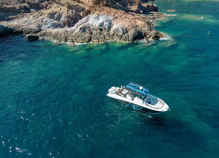 Jeanneau Cap Camarat 10.5 CC: aerial view of boat at anchor in turquoise water beside a rocky headland