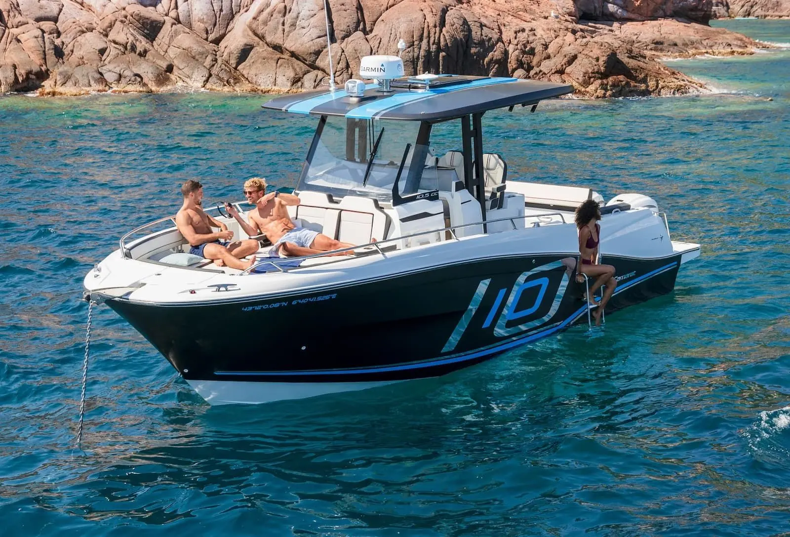Jeanneau Cap Camarat 10.5 CC: at anchor near red rocks, two men on bow seating, woman on side boarding ladder, twin outboards