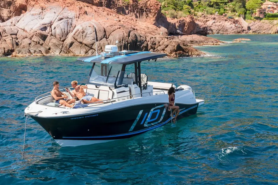 Jeanneau Cap Camarat 10.5 CC: at anchor by rocky coastline, black hull with large 10 graphic, people relaxing on bow seating