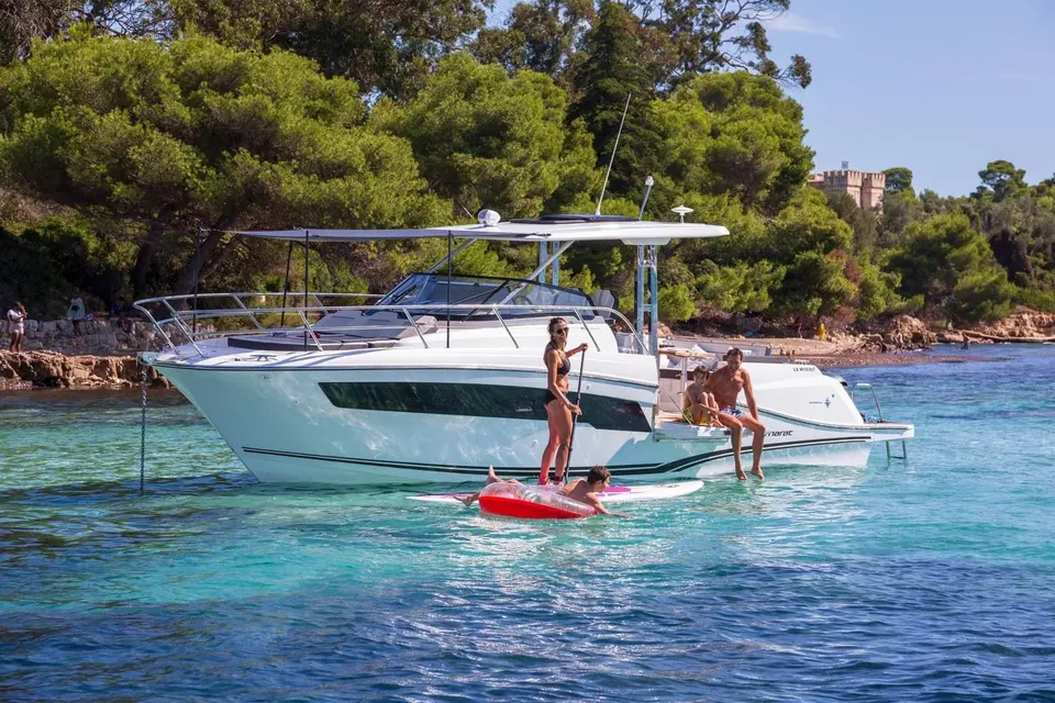 Jeanneau Cap Camarat 10.5 WA Serie 2: at anchor in clear shallow water, people on the bathing platform, paddleboard and inflatable alongside