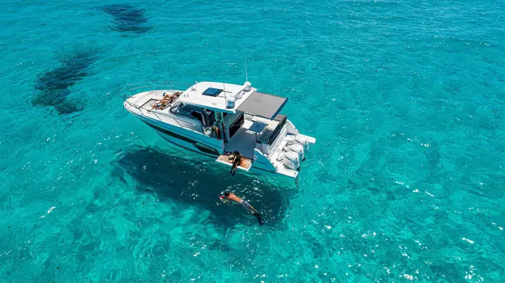 Jeanneau Cap Camarat 12.5 WA: aerial view of the boat at anchor in turquoise water, with a snorkeller swimming beside the hull
