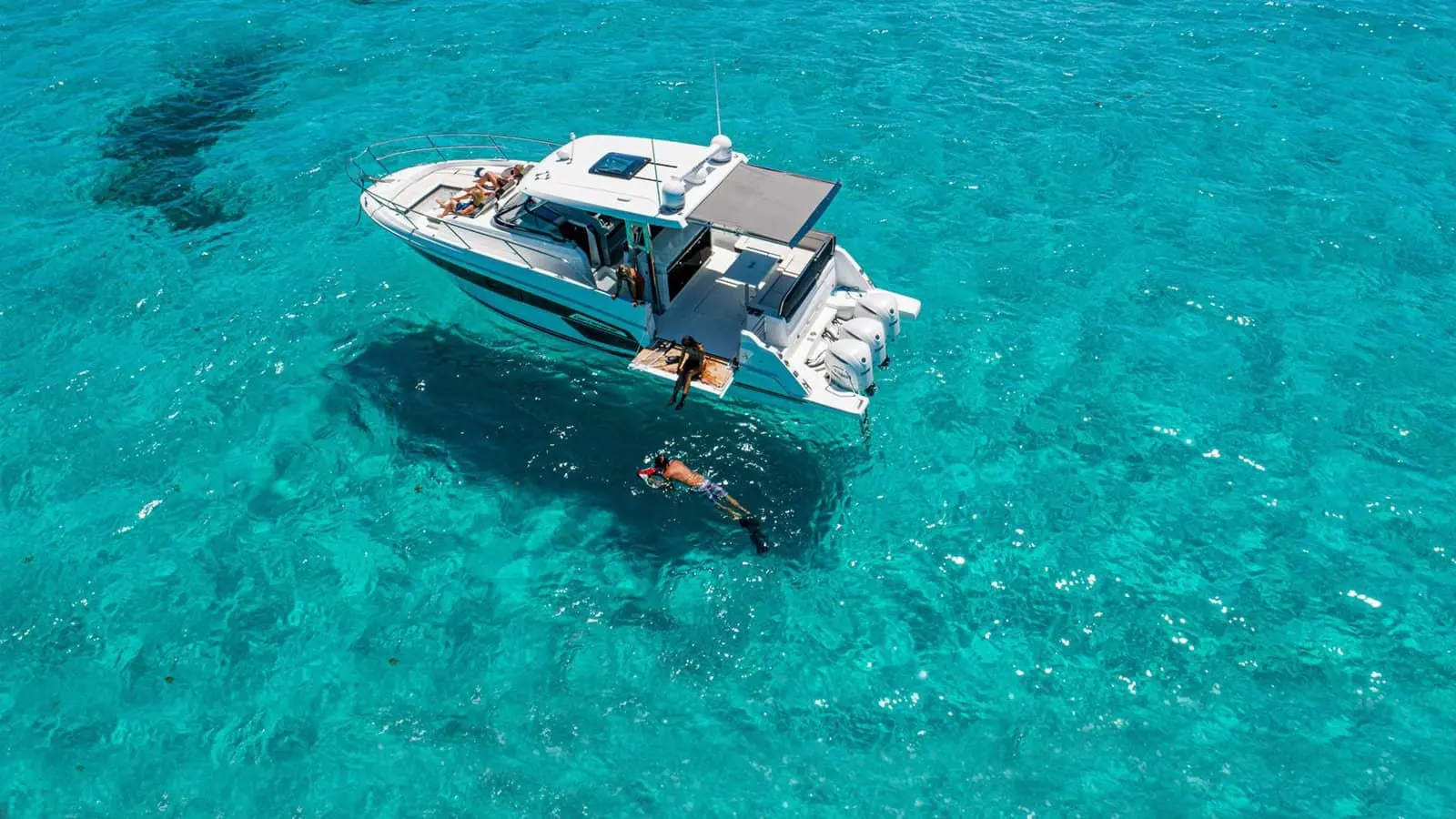 Jeanneau Cap Camarat 12.5 WA: aerial view of the boat at anchor in turquoise water, with a swimmer snorkelling off the stern