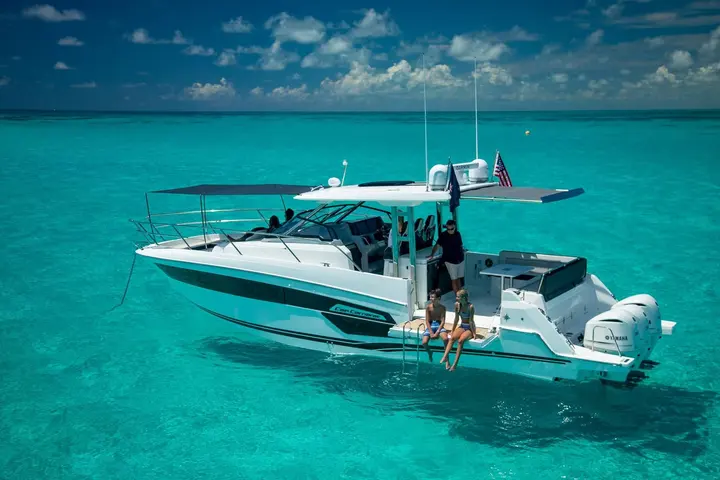 Jeanneau Cap Camarat 12.5 WA: at anchor in clear water, guests sitting on the side bathing platform beneath an extended hardtop sunshade