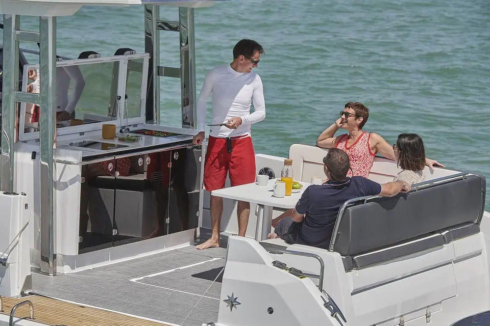 Jeanneau Cap Camarat 12.5 WA: cockpit with outdoor galley unit, table and bench seating, a man standing beside three seated guests