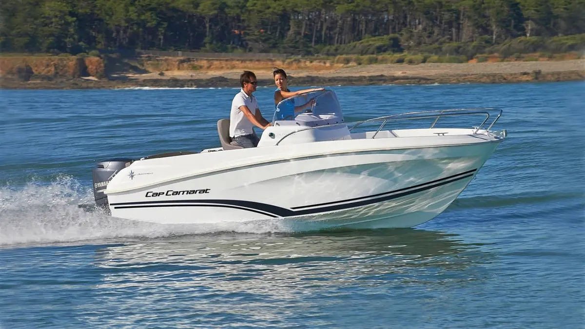 Jeanneau Cap Camarat 5.5 CC: white centre console boat under way with two people at the helm, outboard engine and bow rail
