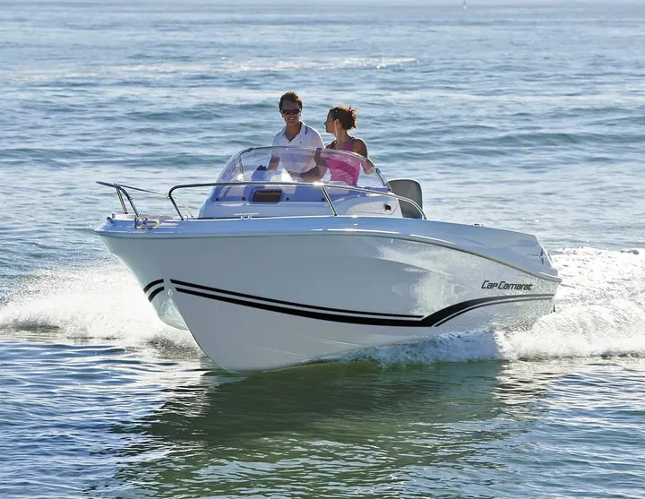 Jeanneau Cap Camarat 5.5 WA: bow view underway at speed, two people standing at the helm behind a curved windscreen