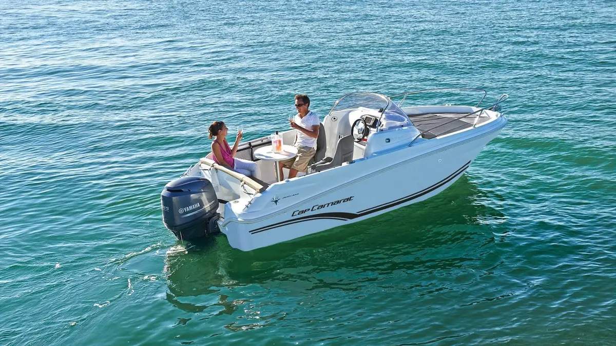 Jeanneau Cap Camarat 5.5 WA: white open boat at rest on calm water, two people seated at a cockpit table behind the helm