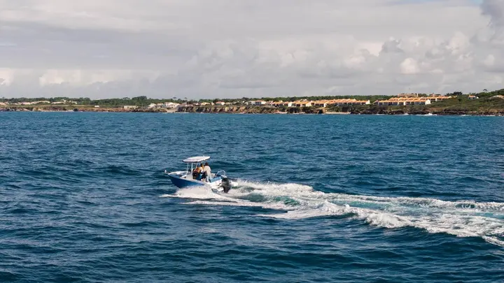 Jeanneau Cap Camarat 6.0 CC: centre console boat with blue hull and T-top under way along a rocky coastline with houses