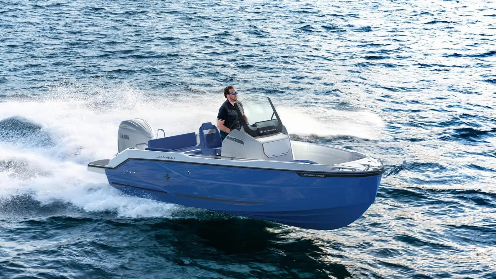 Jeanneau Cap Camarat 6.0 CC: side view under way: blue hull, grey console with windscreen, blue seating and an outboard throwing spray