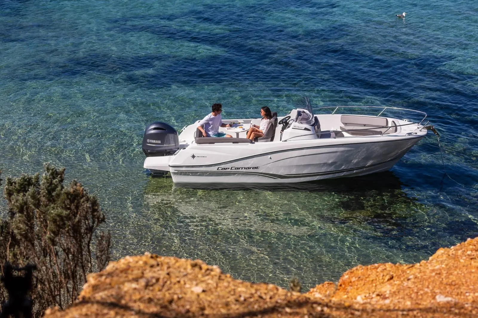 Jeanneau Cap Camarat 6.5 CC: at anchor in clear turquoise water, two people seated at cockpit table, bow seating visible