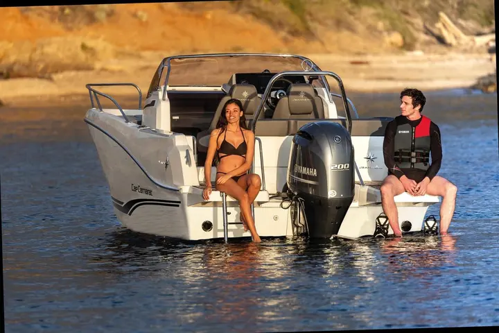 Jeanneau Cap Camarat 6.5 WA: stern view showing twin bathing platforms either side of a Yamaha 200 outboard, two people seated at the transom
