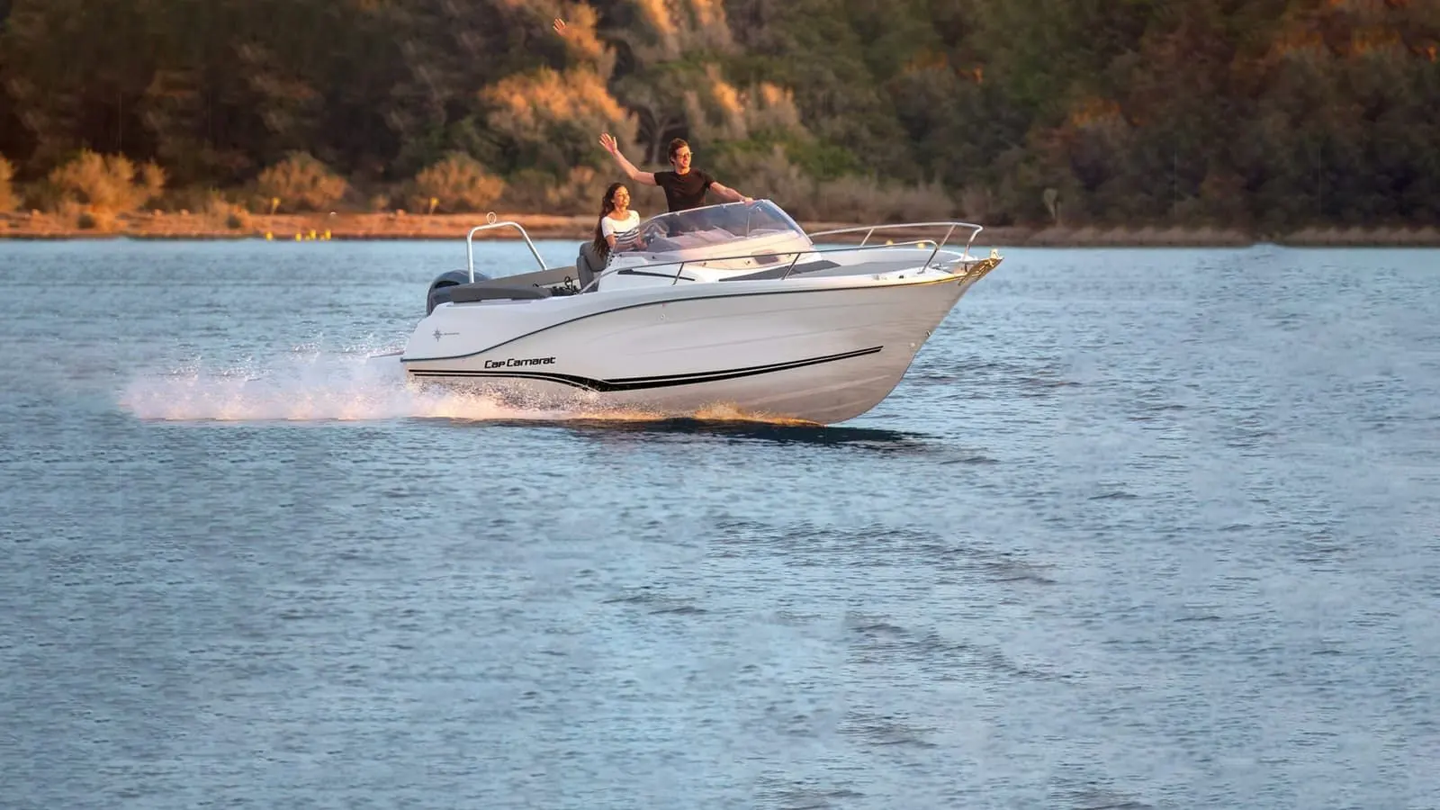 Jeanneau Cap Camarat 6.5 WA: white motorboat under way at speed on calm water, two people standing at the helm waving