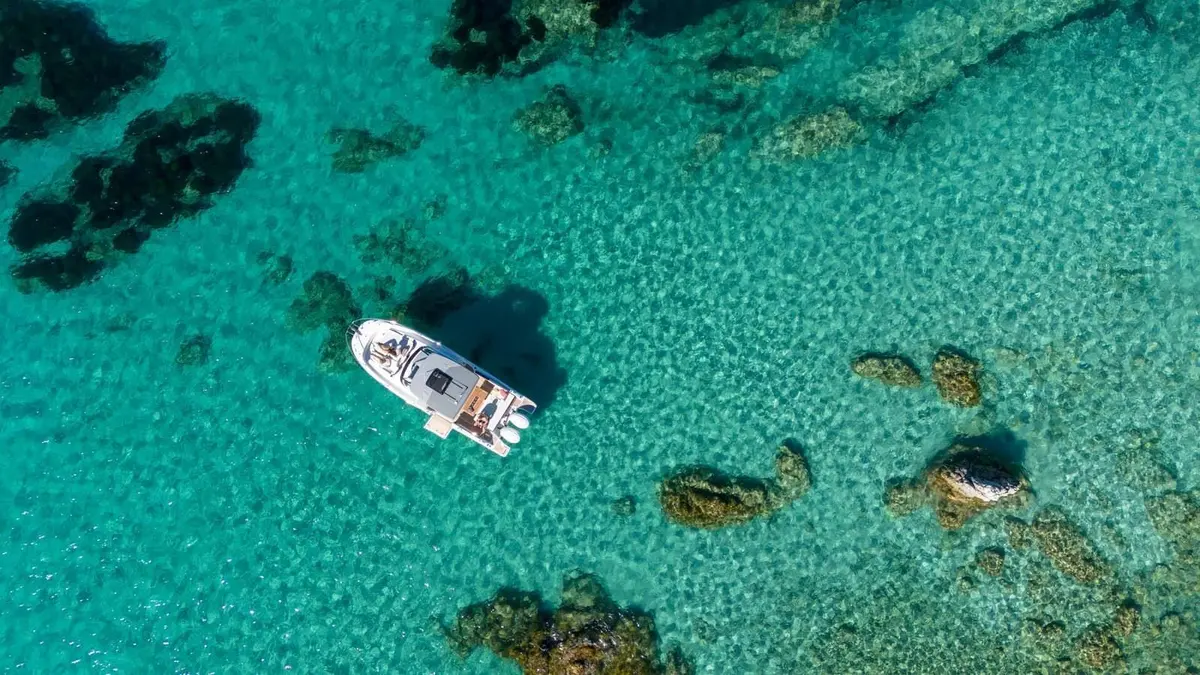 Jeanneau Cap Camarat 9.0 WA Serie 2: aerial view of the boat at anchor in clear turquoise water among dark rocks