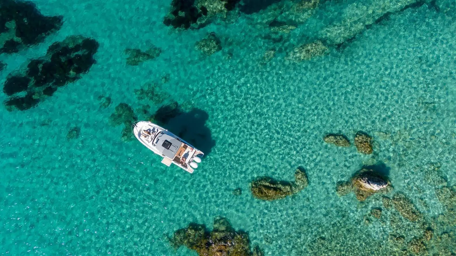 Jeanneau Cap Camarat 9.0 WA Serie 2: aerial view of the boat at anchor in clear turquoise water among dark rocks
