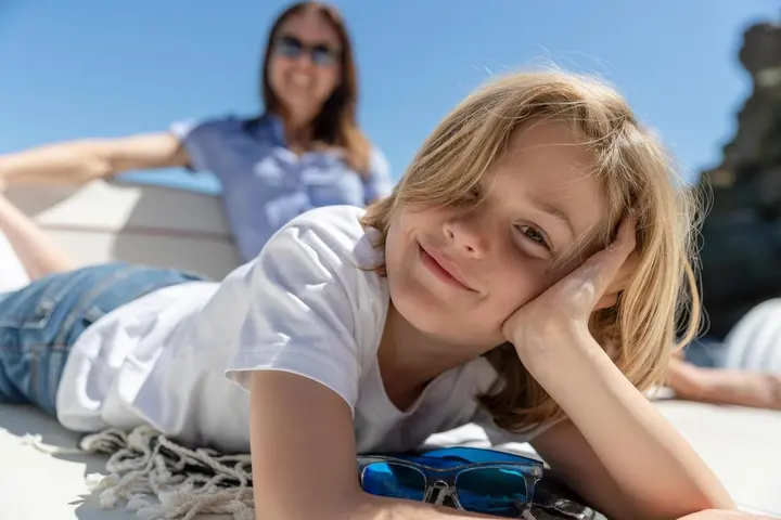 Jeanneau Cap Camarat 9.0 WA Serie 2: close-up of a smiling child lying on the sunbed, woman in sunglasses behind