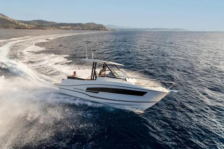 Jeanneau Cap Camarat 9.0 WA Serie 2: white motorboat under way at speed, two people aboard beneath the hardtop, coastline behind