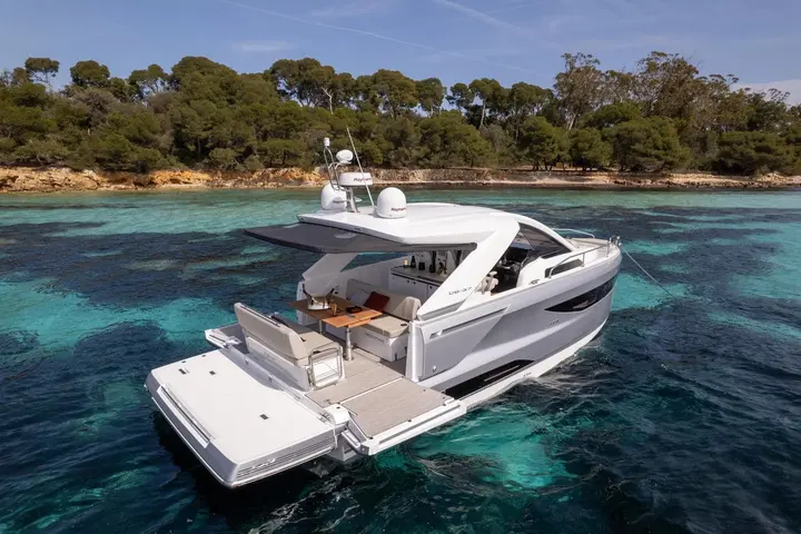 Jeanneau DB 37 IB: stern view at anchor in clear turquoise water, showing bathing platform, aft seating and cockpit table