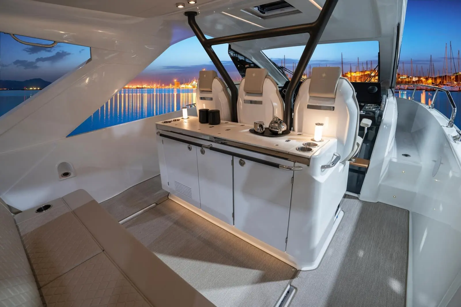 Jeanneau DB 37 OB: cockpit at dusk with cabinet unit, cushioned bench and three helm seats beneath the hardtop