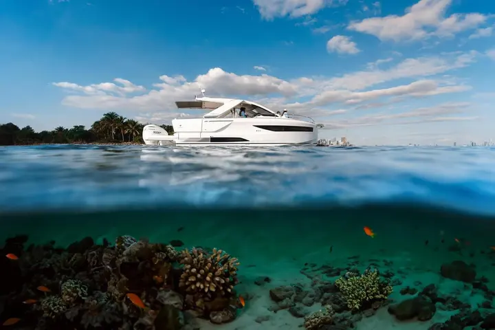 Jeanneau DB 37 OB: white motor yacht at anchor seen from water level, with coral reef and fish below the surface