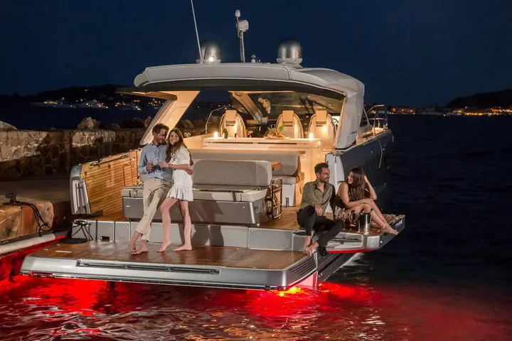 Jeanneau DB 43 IB: stern at night with two couples on the teak bathing platform and cockpit, red underwater lights